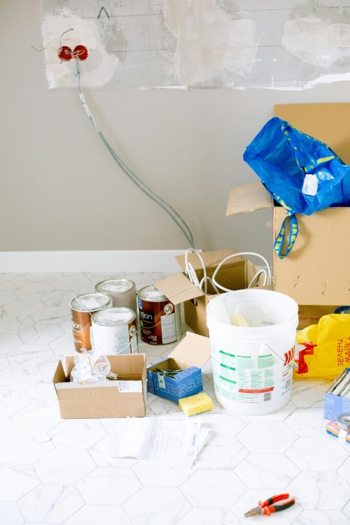 A cluttered room with renovation supplies including paint cans, boxes, and tools.